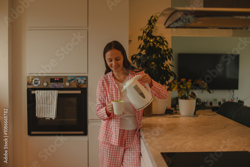 A young woman prepares coffee and tea in the kitchen, enjoying a peaceful moment. Perfect for themes of home life, kitchen activities, and relaxation  photo