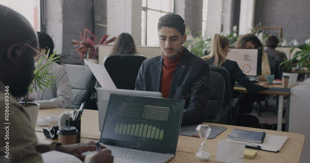 Diverse group of businesspeople working at desks in office using computers and checking documents. Workplace routine and employee concept.