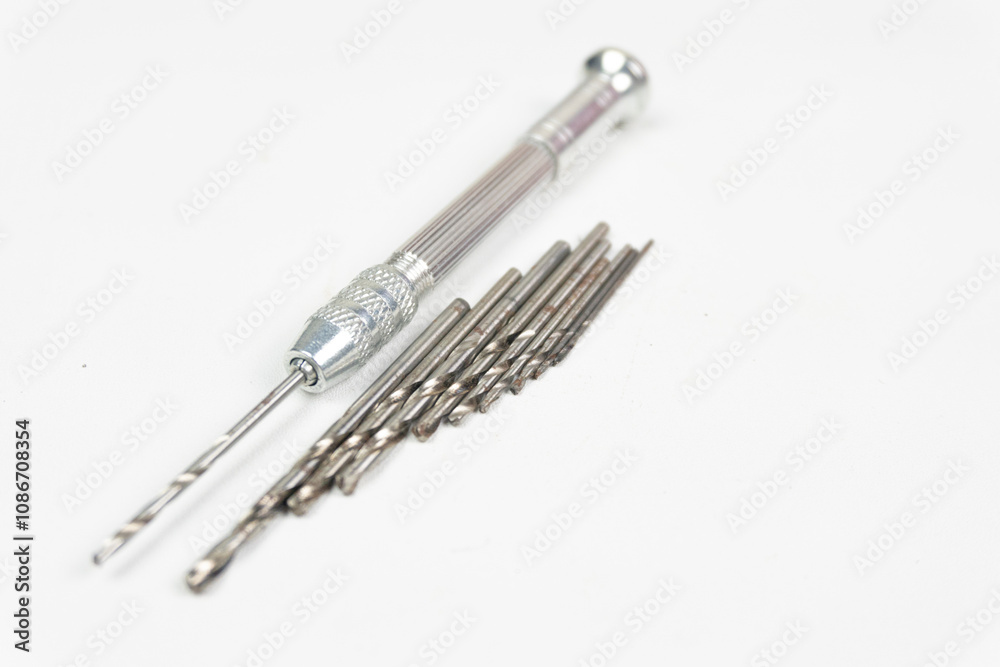 Silver hand drill with several drill bits of different sizes for drilling small objects Silver hand drill with several drill bits of different sizes for drilling small objects