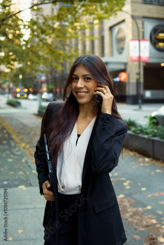 Young professional businesswoman talking on her cell phone while walking on city urban street