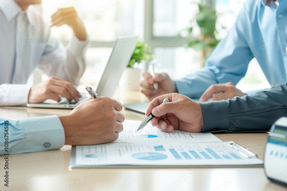 Close-up of hands discussing charts and graphs on documents during a business meeting, with laptops and teamwork in a modern office. Close-up of hands discussing charts and graphs on documents during a business meeting, with laptops and teamwork in a modern office.