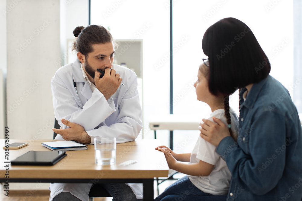 Caucasian male doctor discusses child's health with young girl and mother in clinic. Doctor attentively listens as mother comforts daughter during visit. Caucasian male doctor discusses child's health with young girl and mother in clinic. Doctor attentively listens as mother comforts daughter during visit.