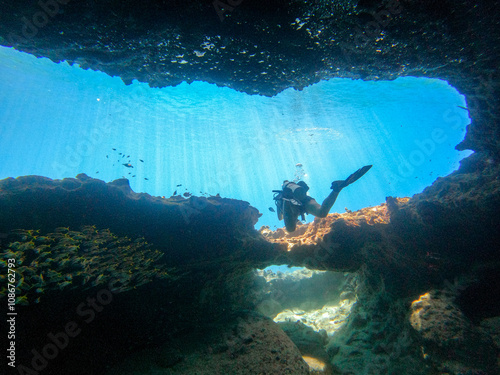 A Scuba diver on a large coral reef cliff in the blue waters of the Caribbean sea in Curacao. This group of fishes is better known as bait ball	 photo