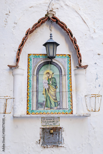 Amalfi, Italy. Votive shrine with Saint Joseph and Baby Jesus painted on ceramic tiles, on the white wall of a house. Vertical image. 2024.09.04.