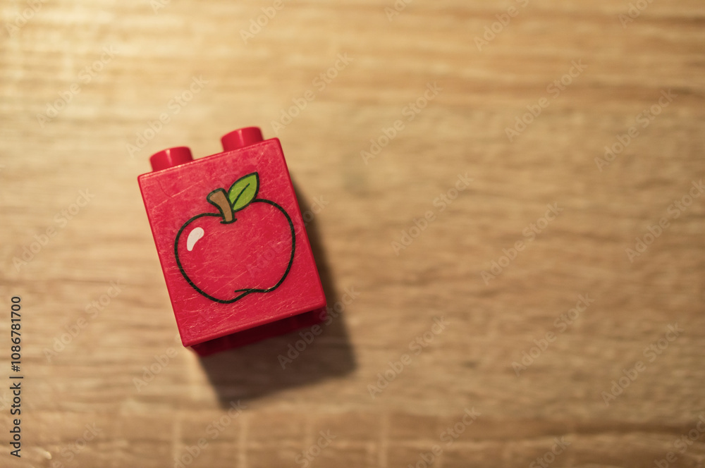 Obraz premium Red Lego Duplo block with an apple icon on a wooden table