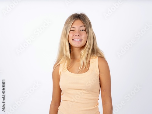 Coquettish Beautiful teen girl wearing sleeveless t-shirt smiling happily, blinking at camera in a playful manner, flirting with you. photo