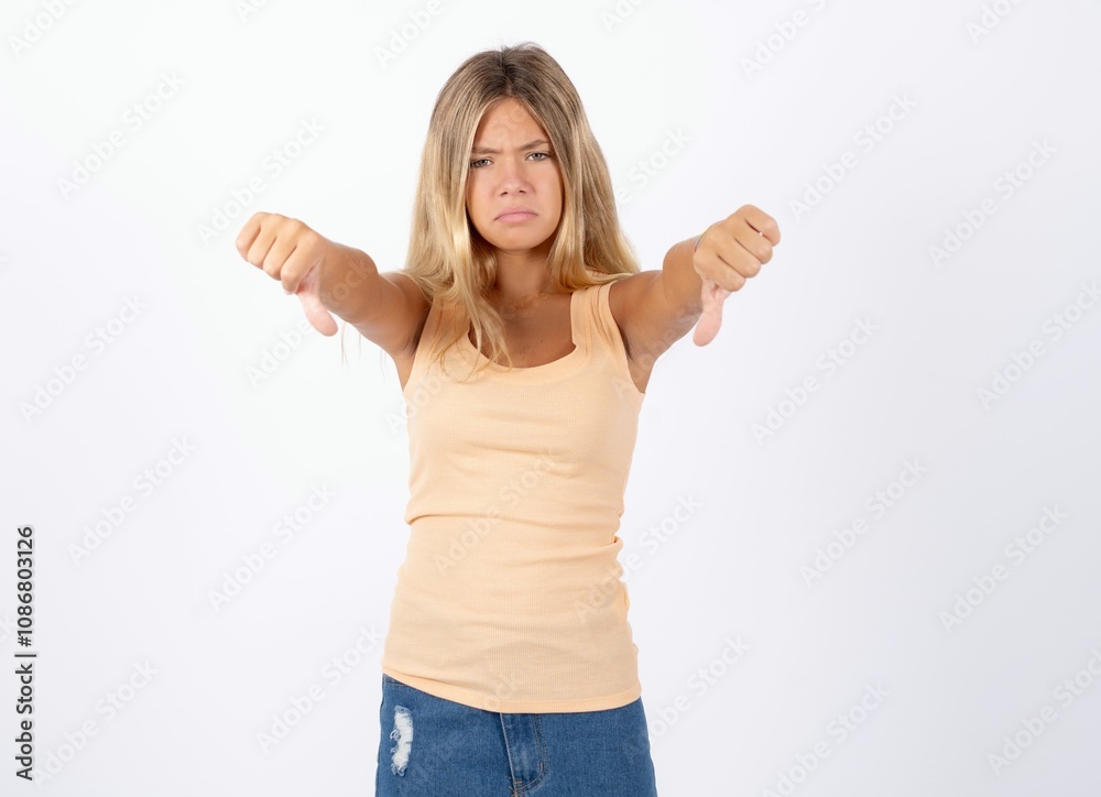 Beautiful teen girl wearing sleeveless t-shirt being upset showing thumb down with two hands. Dislike concept. Beautiful teen girl wearing sleeveless t-shirt being upset showing thumb down with two hands. Dislike concept.