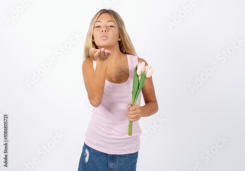 Beautiful teen girl wearing sleeveless t-shirt looking at the camera blowing a kiss with hand on air being lovely and sexy. Love expression.