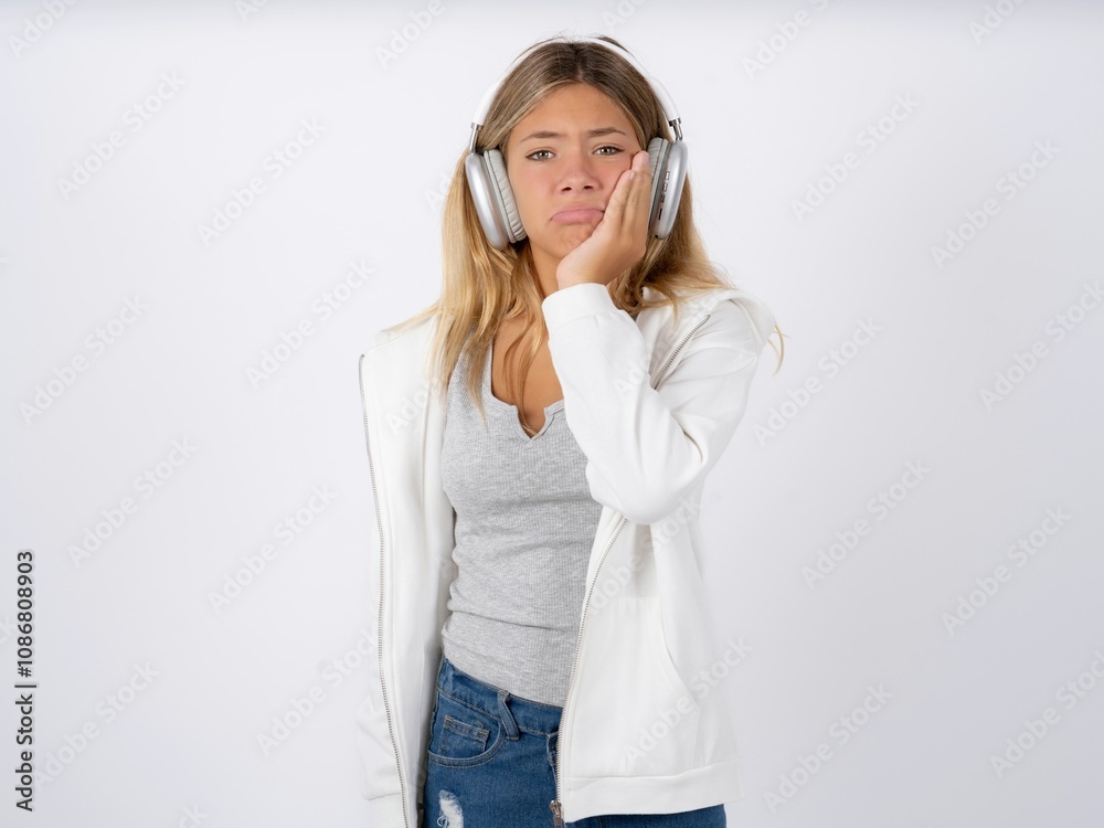 Sad lonely Beautiful teen girl wearing white jacket touches cheek with hand bites lower lip and gazes with displeasure. Bad emotions Sad lonely Beautiful teen girl wearing white jacket touches cheek with hand bites lower lip and gazes with displeasure. Bad emotions