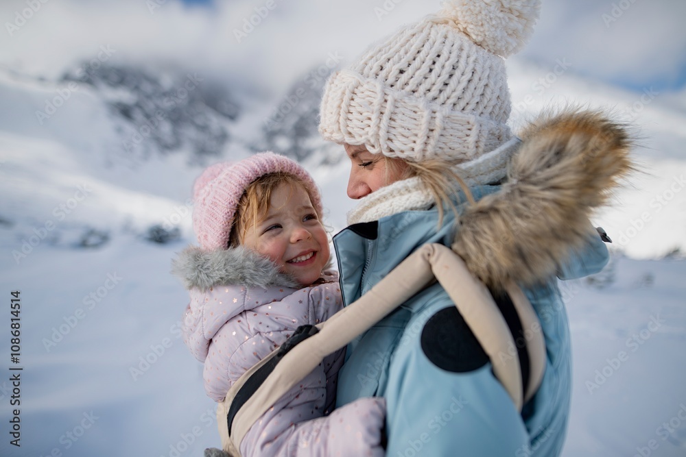 Mother standing in the middle of snowy landscape with daughter in baby carrier. Mom and girl enjoying winter holiday in the mountains. Mother standing in the middle of snowy landscape with daughter in baby carrier. Mom and girl enjoying winter holiday in the mountains.