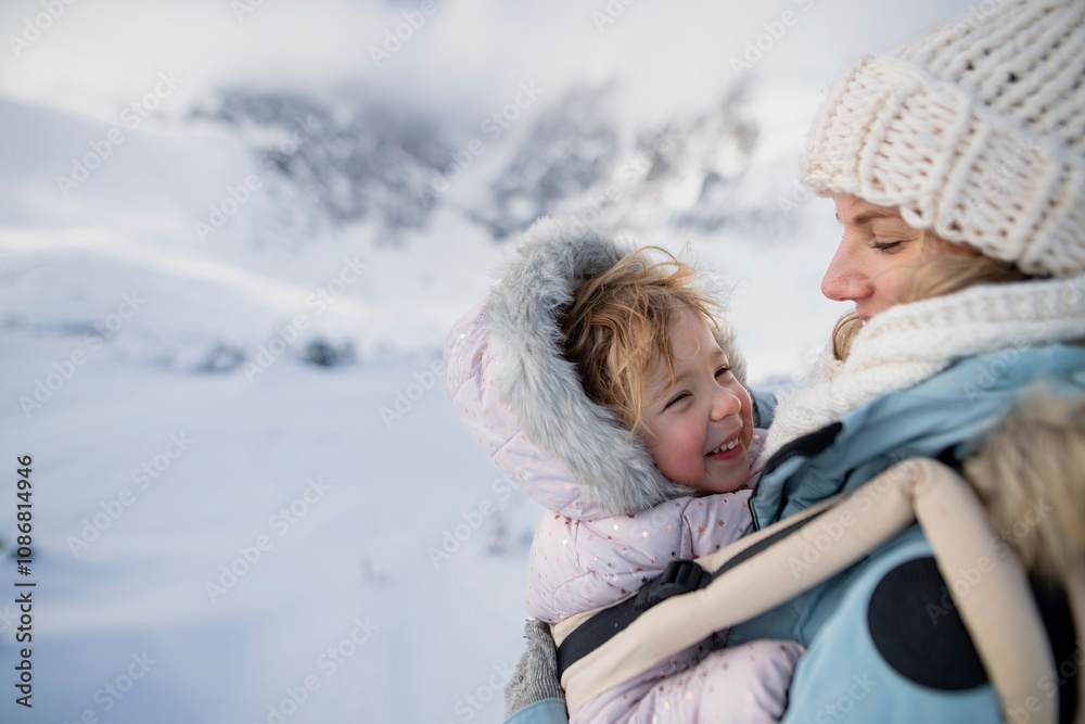 Mother standing in the middle of snowy landscape with daughter in baby carrier. Mom and girl enjoying winter holiday in the mountains. Mother standing in the middle of snowy landscape with daughter in baby carrier. Mom and girl enjoying winter holiday in the mountains.
