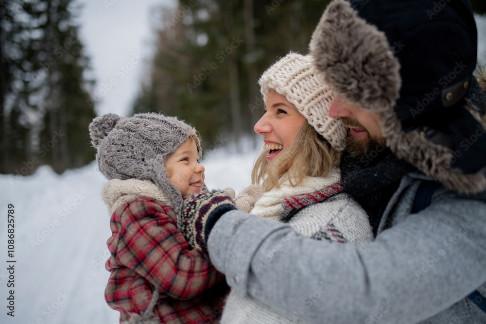 Fototapeta premium Young family is enjoying winter holiday in the mountains, standing in the middle of snowy forest.