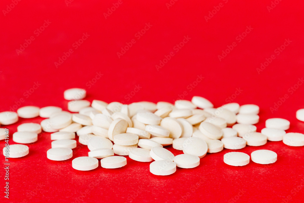 Heap of white pills on colored background. Tablets scattered on a table. Pile of red soft gelatin capsule. Vitamins and dietary supplements concept Heap of white pills on colored background. Tablets scattered on a table. Pile of red soft gelatin capsule. Vitamins and dietary supplements concept