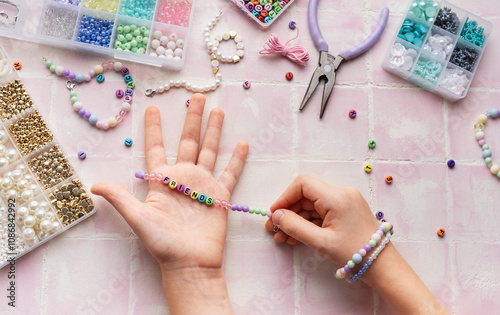 Child making beaded bracelets at home on pink tiled table