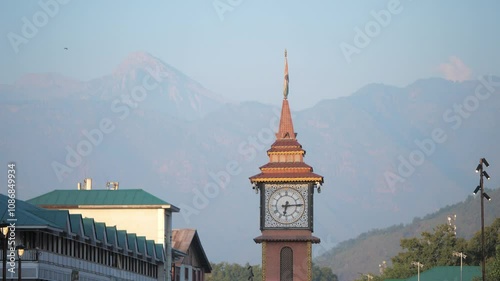 A Close shot of clock tower at Lal chowk surrounded by houses or building with a view of towering snow capped Himalaya mountains visible in the background, Srinagar, Jammu and Kashmir, India