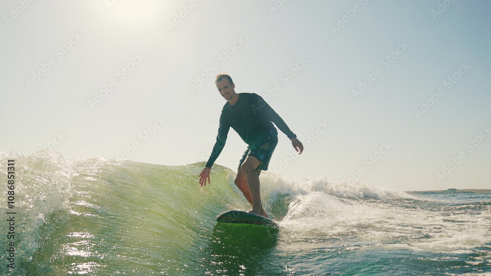 Sportsman performs tricks while balancing on a wakeboard. Wakeboarding behind a motorboat on the surface of the water. The scene conveys the dynamics, speed and adrenaline of water extreme sports Sportsman performs tricks while balancing on a wakeboard. Wakeboarding behind a motorboat on the surface of the water. The scene conveys the dynamics, speed and adrenaline of water extreme sports