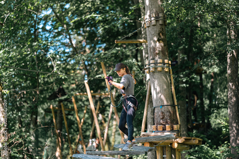 An individual skillfully navigating a challenging tree climbing course amidst vibrant greenery and excitement An individual skillfully navigating a challenging tree climbing course amidst vibrant greenery and excitement