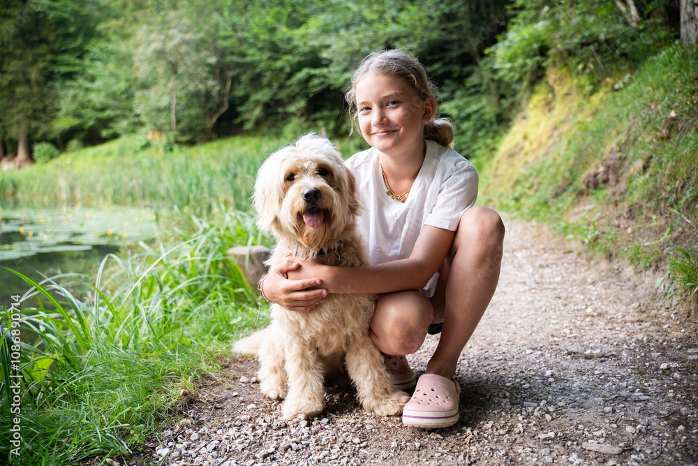 Smiling girl crouching with golden doodle dog in forest Smiling girl crouching with golden doodle dog in forest