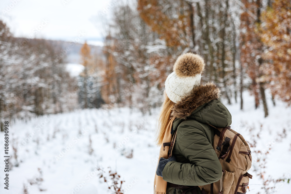 Woman in winter jacket and knitted bobble hat with backpack hiking in snowy nature. Forest therapy Woman in winter jacket and knitted bobble hat with backpack hiking in snowy nature. Forest therapy