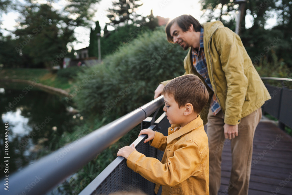 Father and son standing on bridge and looking at lake in park Father and son standing on bridge and looking at lake in park