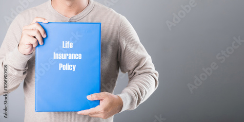 A man holds a blue life insurance policy booklet against a gray background, symbolizing the importance of planning and securing financial protection for the future photo