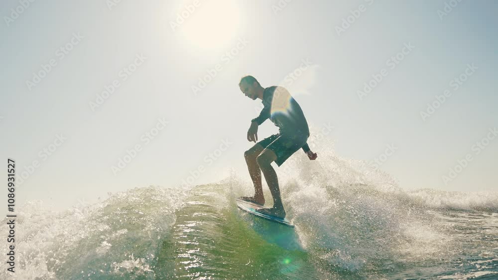 Sportsman performs tricks while balancing on a wakeboard. Wakeboarding behind a motorboat on the surface of the water. The scene conveys the dynamics, speed and adrenaline of water extreme sports Sportsman performs tricks while balancing on a wakeboard. Wakeboarding behind a motorboat on the surface of the water. The scene conveys the dynamics, speed and adrenaline of water extreme sports