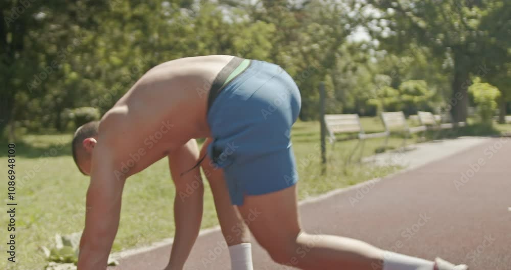 A muscular man rests on a park path after a fitness workout. He picks up his towel and walks toward outdoor exercise equipment to begin his training. A muscular man rests on a park path after a fitness workout. He picks up his towel and walks toward outdoor exercise equipment to begin his training.