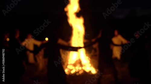 Unrecognizable people dance circle around a big campfire at night. Blurred shot 4K
