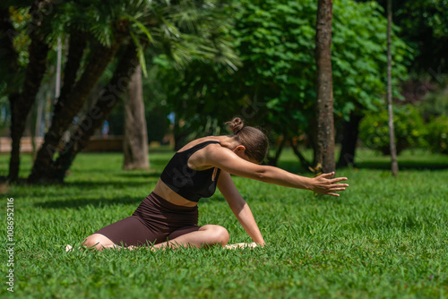 Young woman in sports clothes does yoga, smart fitness, Pilates, stretching on the lawn on a mat in the park. Concept of health, well-being