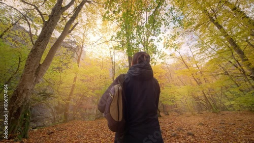 Young wooman standing into the autumn forest and look on tree crowns.