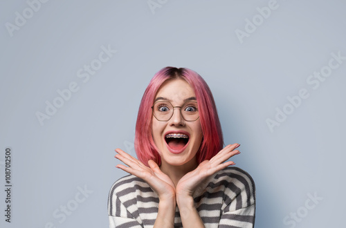 Excited surprised shock astonished very happy pink woman wear braces, tooth brackets eye glass spectacles, open mouth, hold hands palms near face, isolated blue background. Mega sales ad concept