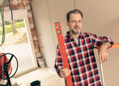 Happy, handsome, caucasian, handyman in a plaid shirt. Builder holding a level in a renovated home interior.