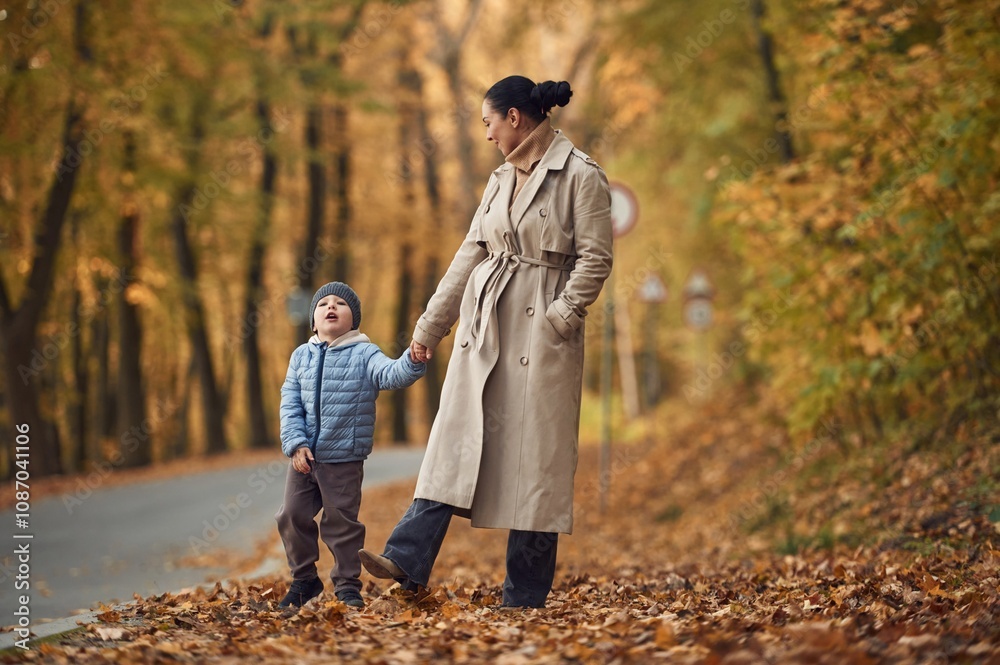 Fototapeta premium Mother with her son are having a walk in autumn forest near the road