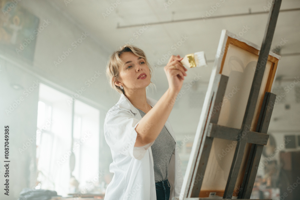 Young female artist working on a painting by the window Young female artist working on a painting by the window
