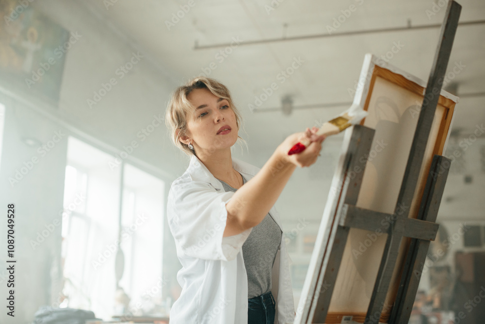 Young female artist working on a painting by the window Young female artist working on a painting by the window