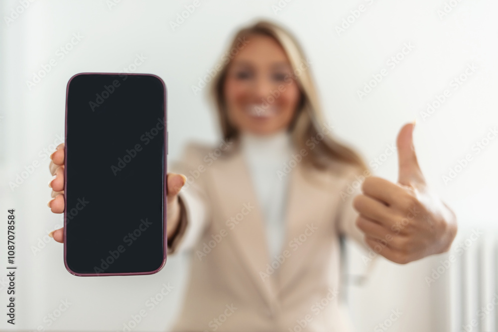 A beautiful and smiling young Asian businesswoman sits at her desk, showing her thumb up and holding a smartphone white screen mockup in a horizontal position. isolated white background. A beautiful and smiling young Asian businesswoman sits at her desk, showing her thumb up and holding a smartphone white screen mockup in a horizontal position. isolated white background.