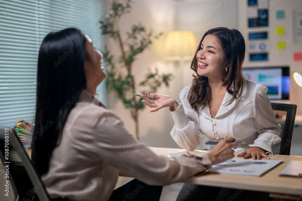 Two women are sitting at a desk talking Two women are sitting at a desk talking