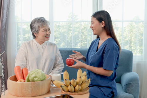 Female nutritionist holds apple while consult about healthy foods to Asian senior woman. Happy elderly grandma listens to advice from medical nurse on improving diet. Elderly healthcare and nutrition