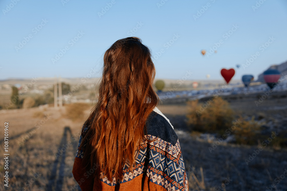 Vibrant woman with fiery red hair in front of colorful hot air balloons floating over a scenic field Vibrant woman with fiery red hair in front of colorful hot air balloons floating over a scenic field