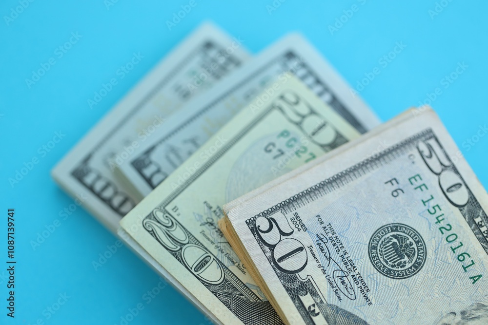 Big amount of hundred, fifty and twenty dollar bills in thick stack lies on bright blue color paper background Big amount of hundred, fifty and twenty dollar bills in thick stack lies on bright blue color paper background