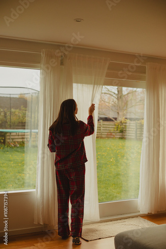 Woman opening curtains in cozy home, letting sunlight into the bedroom. Perfect for concepts of fresh starts, relaxation, or home lifestyle. photo