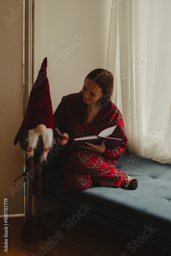  Woman in cozy plaid pajamas smiling while hugging a Christmas gnome. Perfect for holiday themes, winter coziness, and family celebration concepts.  photo