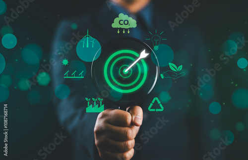 Green Energy and Sustainability Concept. A man holding a magnifying glass focusing on a target with a leaf, surrounded by green energy and sustainability icons on a green background. Carbon footprint. photo