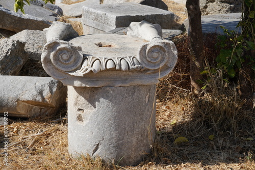 Scattered across the grassy expanse lie elements of ancient architecture: stone blocks and column fragments, remnants of the Greek and Roman empires, preserved to this day in Kos, Greece. photo