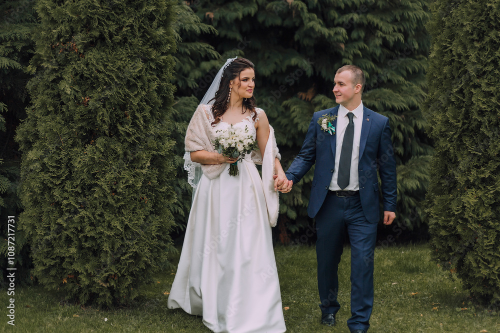 A bride and groom are walking together in a garden. The bride is wearing a white dress and a veil, while the groom is wearing a blue suit. They are holding hands and appear to be happy and in love A bride and groom are walking together in a garden. The bride is wearing a white dress and a veil, while the groom is wearing a blue suit. They are holding hands and appear to be happy and in love