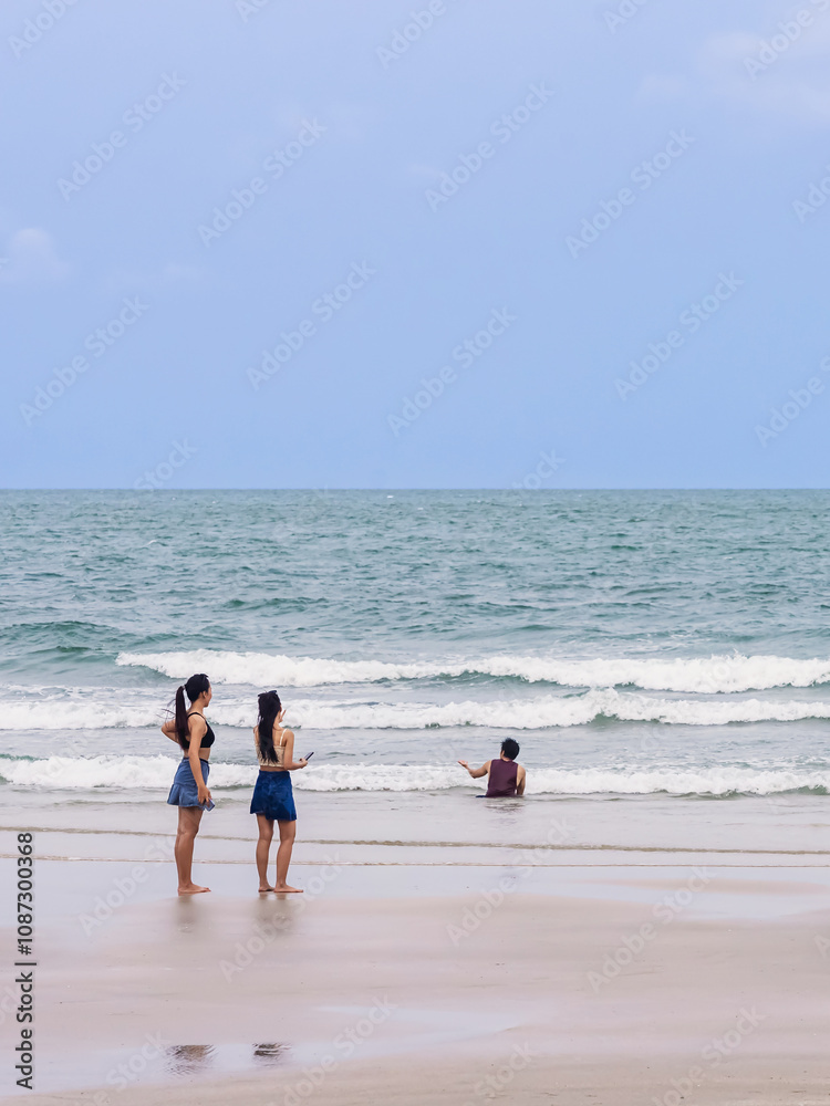 Back view of happy carefree women using mobile phone at beach. Woman friends using smartphone at seaside. Beautiful lovely two women spending time at beach. Concept of travel, tourism and vacation. Back view of happy carefree women using mobile phone at beach. Woman friends using smartphone at seaside. Beautiful lovely two women spending time at beach. Concept of travel, tourism and vacation.