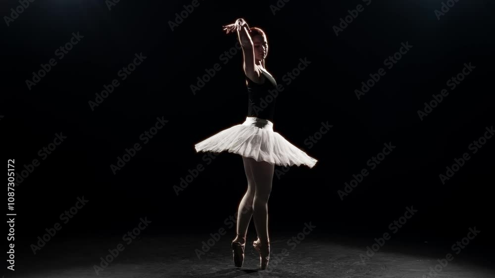 Dramatic and elegant dance of beautiful ballerina in darkness, slow motion shot. Graceful ballet dancer dancing alone on stage with bright soffit, female silhouette in contour light, classical art