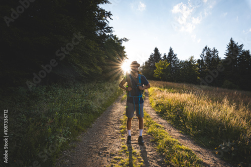 Hiker with backpack standing on a sunlit trail in the Beskydy Mountains, Czech Republic. Embracing adventure and nature, surrounded by forests and open meadows at sunset