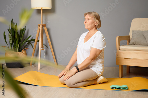 Senior woman practicing yoga in a calm indoor setting while sitting on a yellow mat, focused on mindfulness and relaxation during morning routine photo