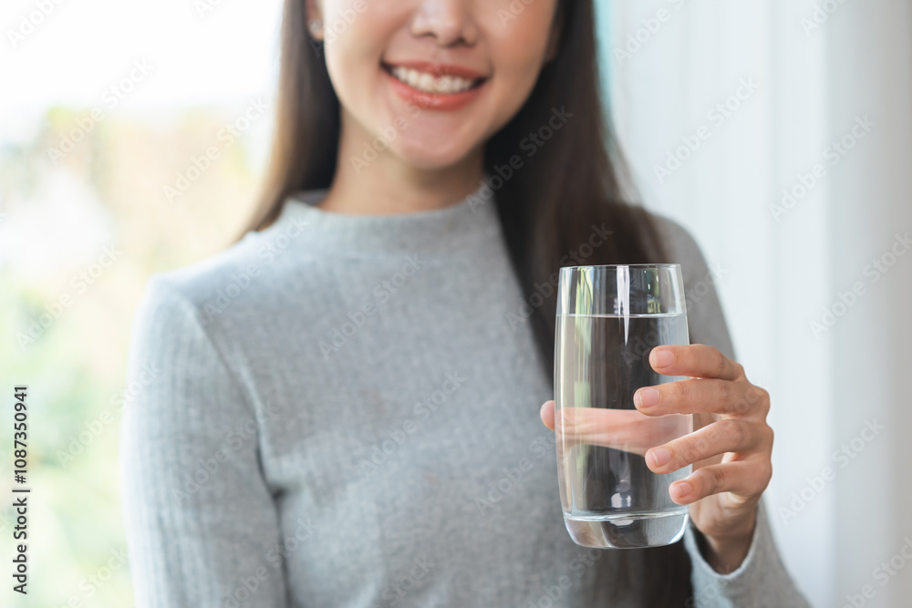 Happy beautiful, asian young woman, girl drinking, sip fresh glass of water for hydration of body, holding transparent glass in her hand, thirsty at home. Health care, healthy lifestyle concept.
